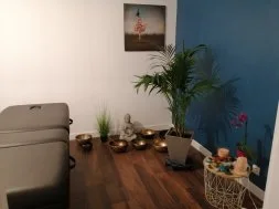 L’espace de soins du cabinet : table de massage, bols tibétains, statuette de Bouddha, palmier et mur bleu